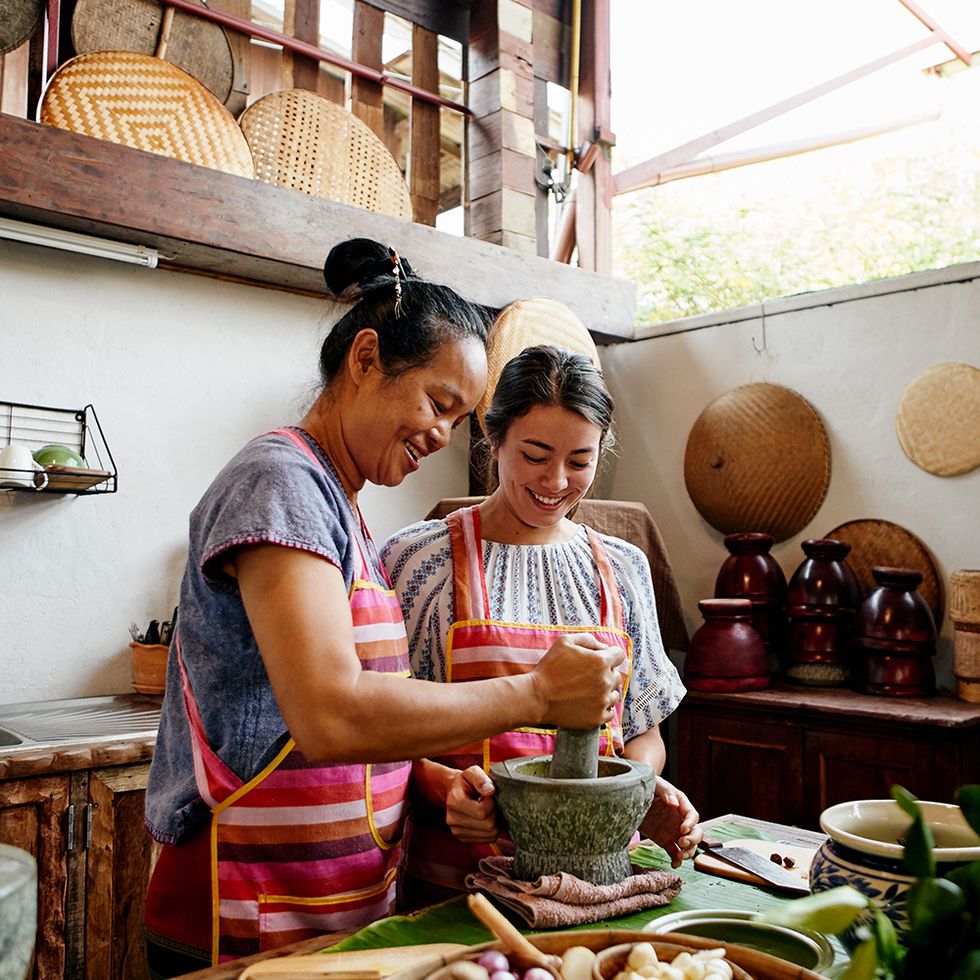 a photo of one woman showing another how to cook using a mortar and pestle