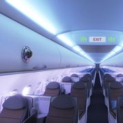 an empty airplane cabin with a device that looks like a video camera attached to one of the overhead compartments