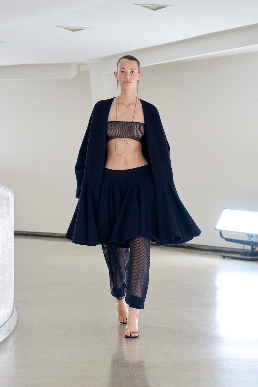 a model walks down a fashion runway wearing a dark outfit with a cropped top and a flowing skirt