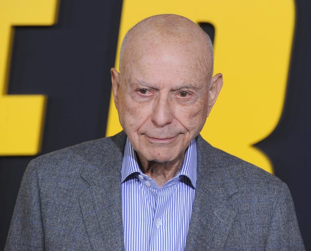 alan arkin, wearing a gray suit jacket and purple striped shirt