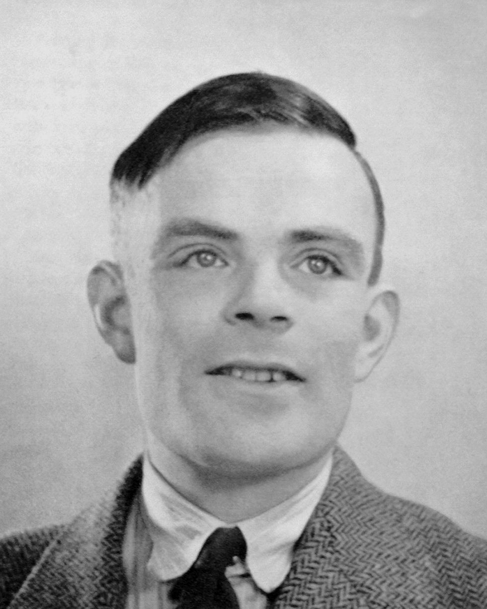 alan turing wearing a suit and tie and smiling for a photo circa 1947