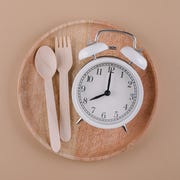 Alarm clock on wooden plate with cutlery. Concept of intermittent fasting, diet and weight loss. Flat lay alarm clock on wooden plate with cutlery concept of intermittent fasting diet and weight loss flat lay