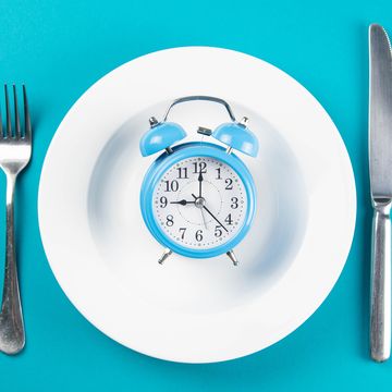 alarm clock with fork and knife on the white plate on blue table time to eat, breakfast, lunch time and dinner concept
