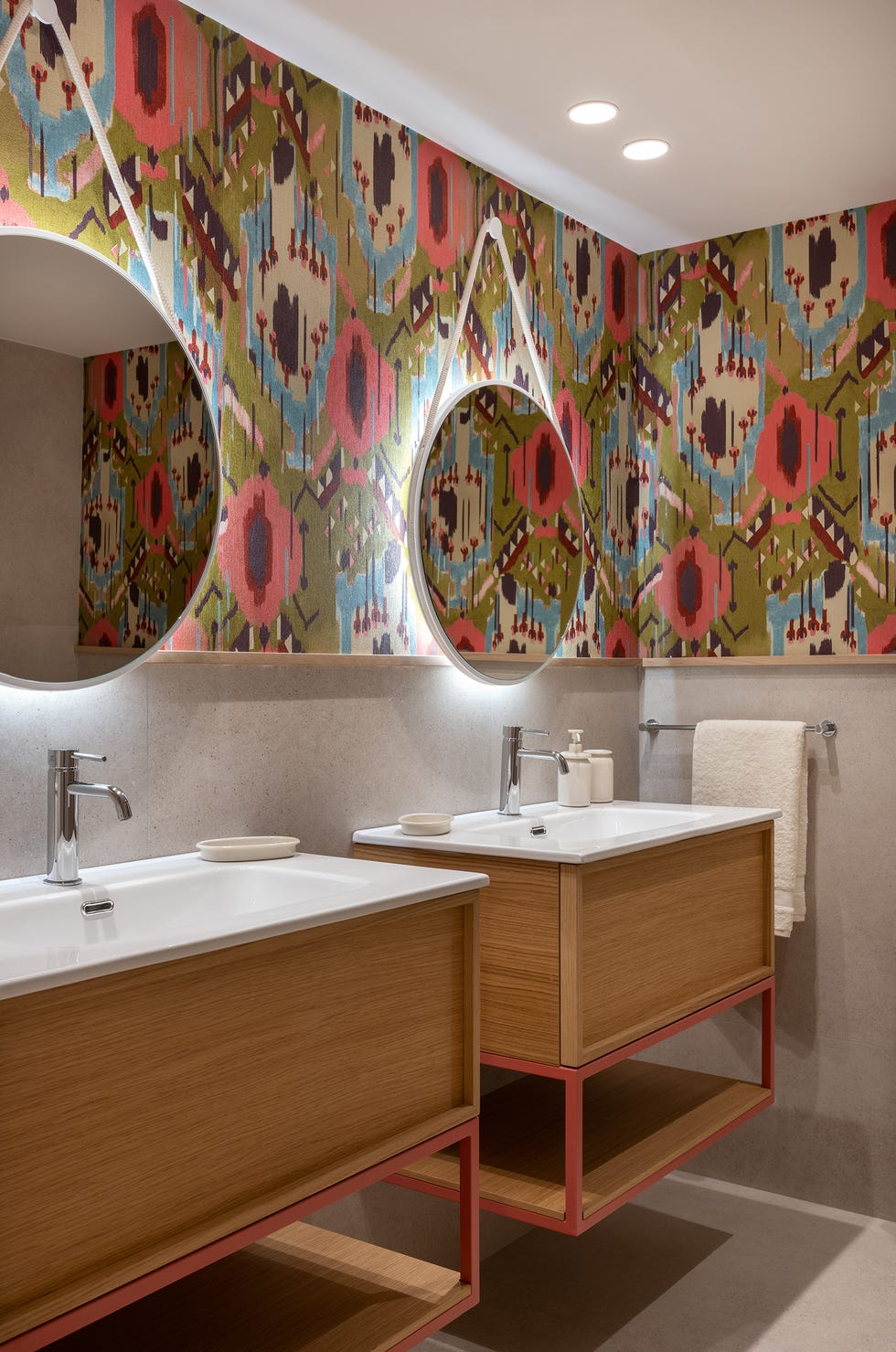 baño con dos muebles de madera y papel pintado con motivos abstractos