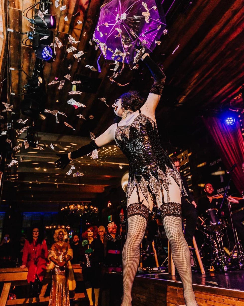 drag queen performing on stage, throwing money in a sparkling outfit dancing with a purple umbrella at alberts schloss on nye