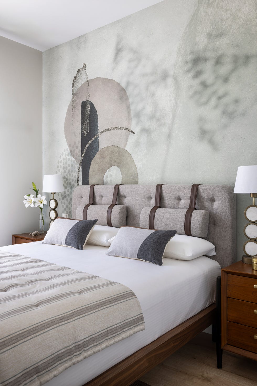 cabecero de cama tapizado en gris con tiras de cuerpo y papel pintado con motivos abstractos