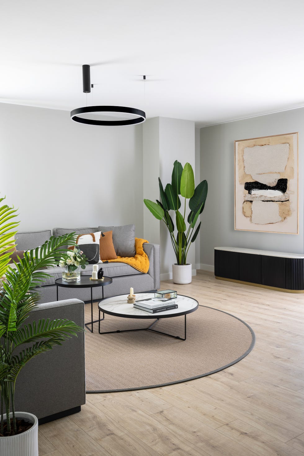 sofá gris, mesas tipo nido redondas y cuadro sobre el mueble de tv