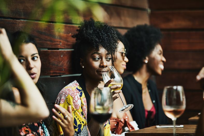a stylish young black woman enjoying a glass of wine with friends at a bar