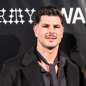 Two individuals posing at an event with a black background displaying branding