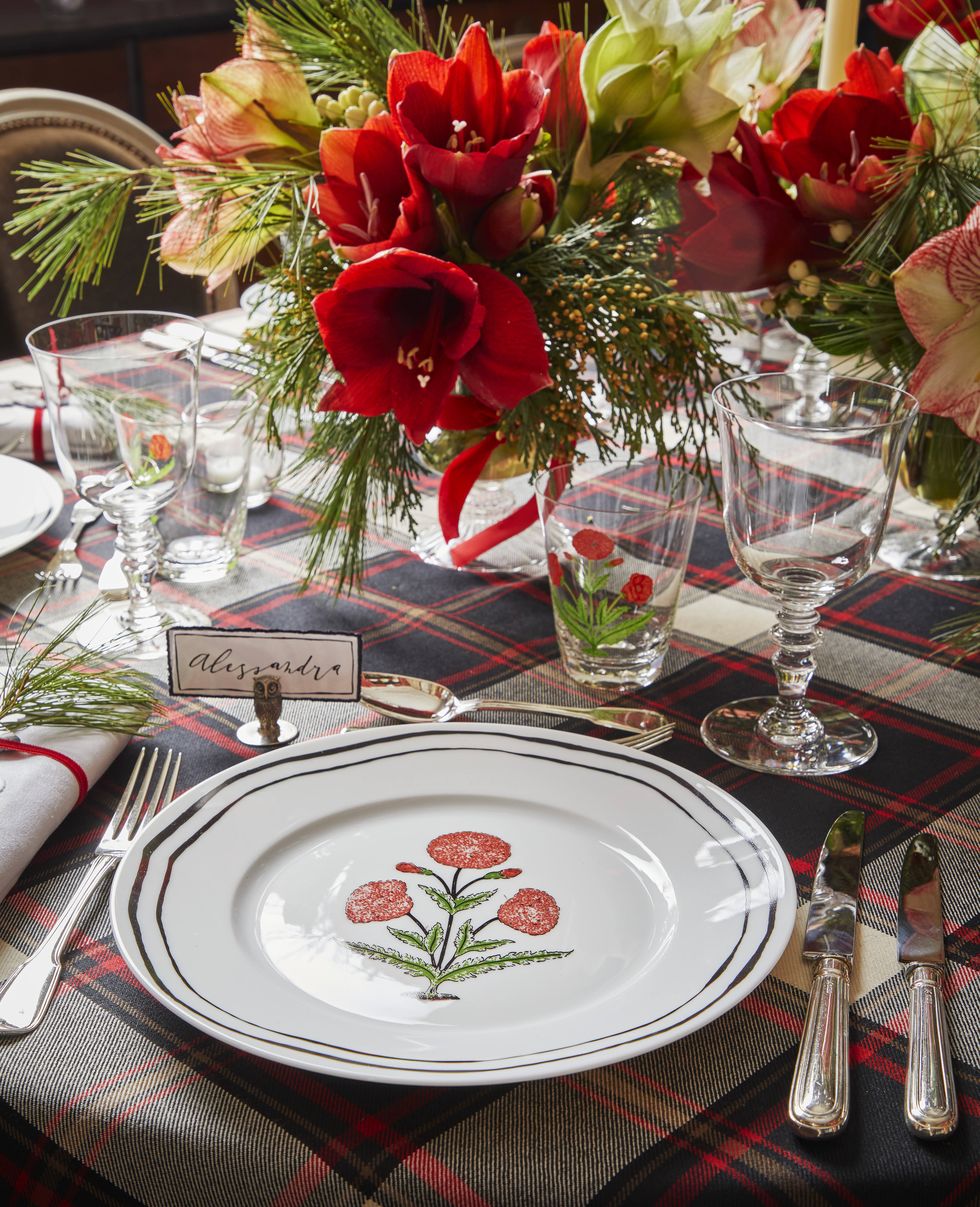 a dining table set for the holidays with a plaid table cloth and red and white plates and flowers