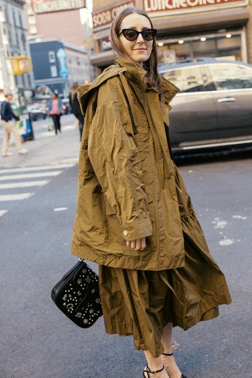 person wearing a loose olivegreen jacket with a large hood and carrying a stylish handbag
