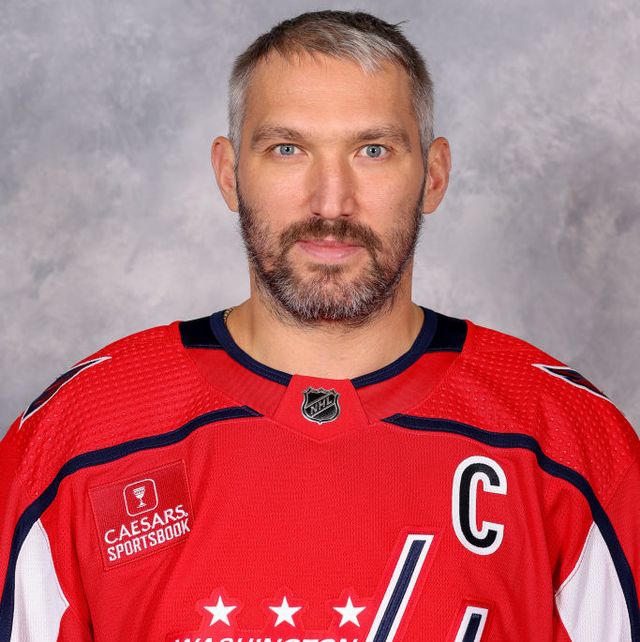 alex ovechkin looks at the camera with a slight smile, he wears a red hockey jersey with navy and white accents