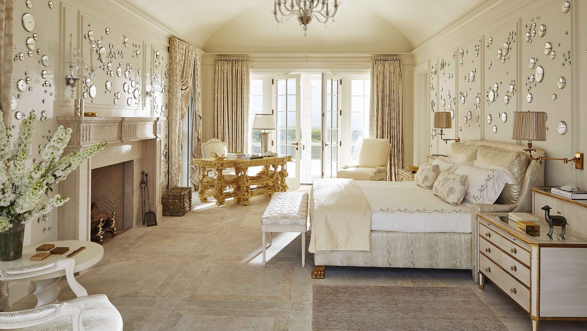 an ivory and gold master bedroom with a fireplace and large bed with doors opening out to the ocean