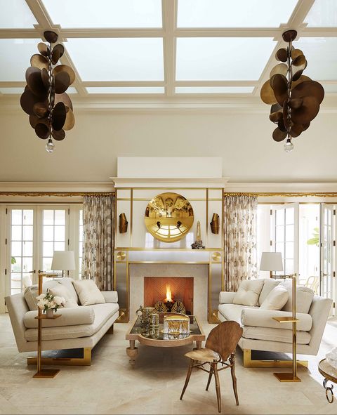 a pair of custom cantilevered sofas are upholstered in white velvet  the full room is decorated in ivory and gold accents