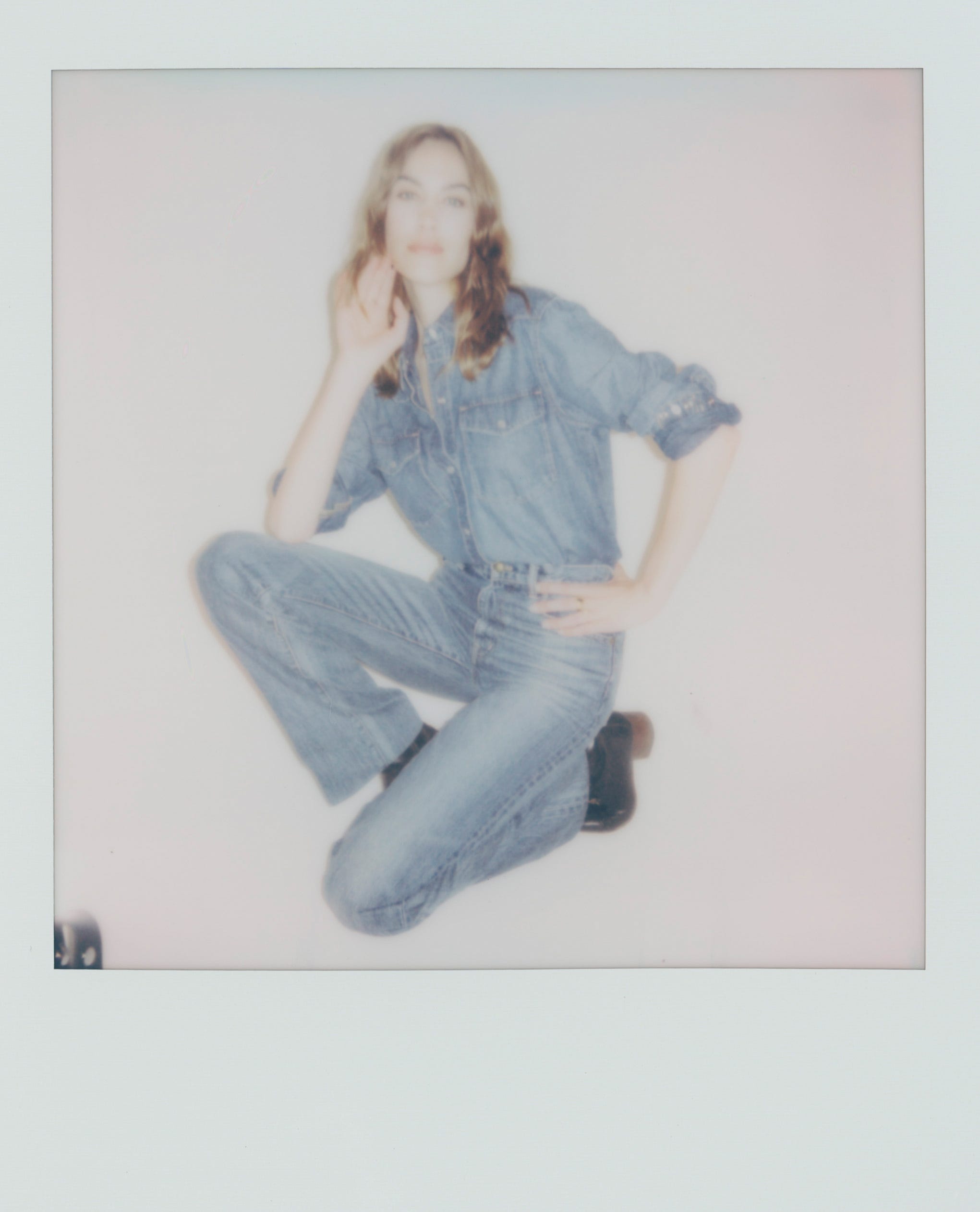 a woman wearing a denim shirt and jeans posing in a crouch