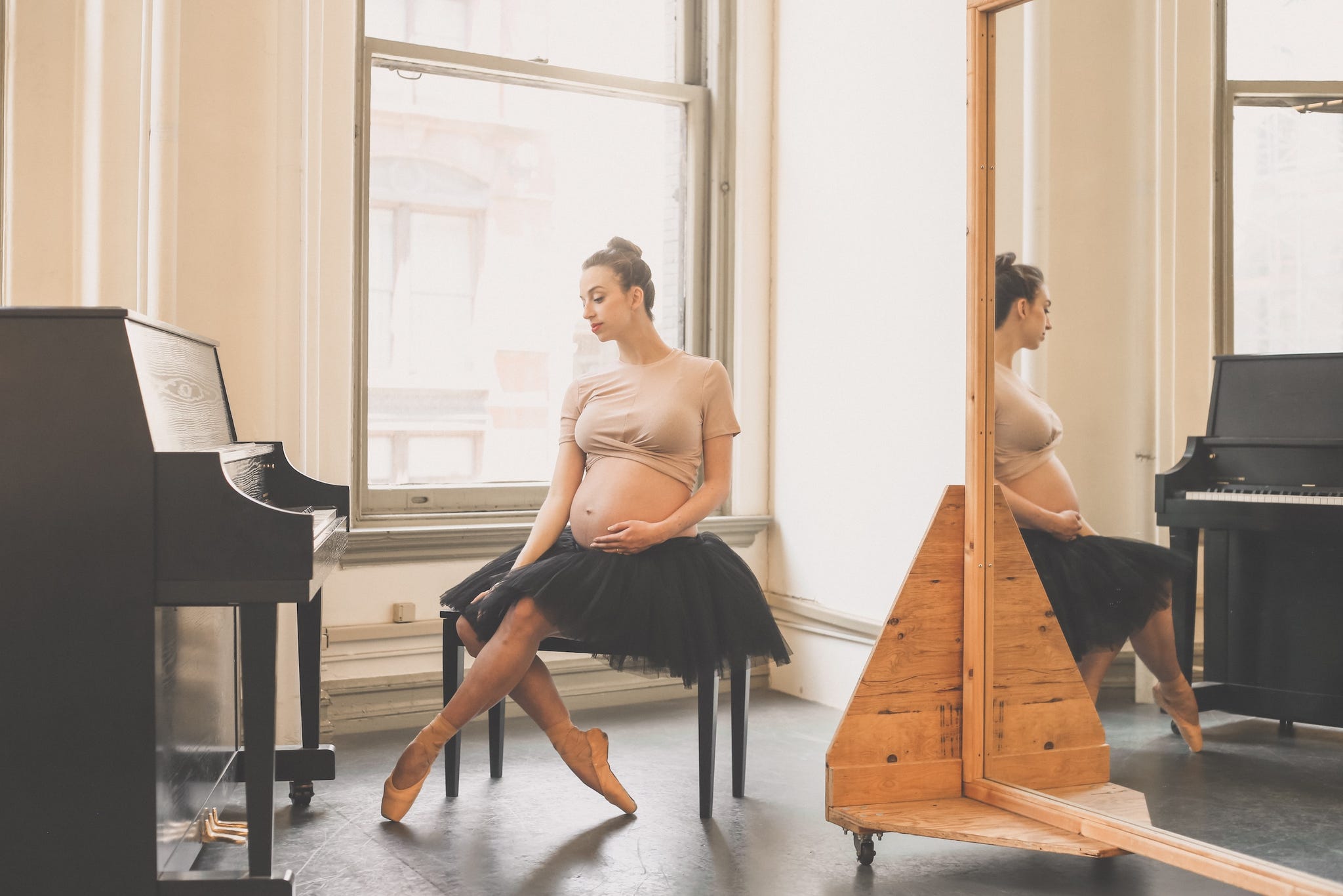a pregnant woman in a tutu seated near a piano and mirror