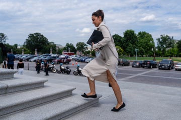 alexandria ocasio cortez ascending a set of stone steps carrying a folder and a water bottle