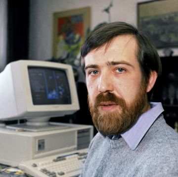 alexey pajitnov, wearing a blue gray sweater, looks directly into the camera while sitting at a desk, with a computer in the background