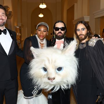 serena williams, alessandro michele, and jared leto pose for a photo in formal attire inside a building, in front of michele is an oversized head from a cat costume