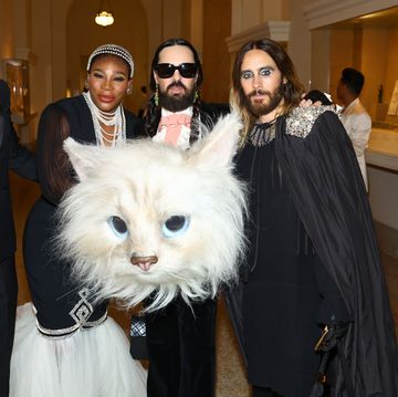 serena williams, alessandro michele, and jared leto pose for a photo in formal attire inside a building, in front of michele is an oversized head from a cat costume