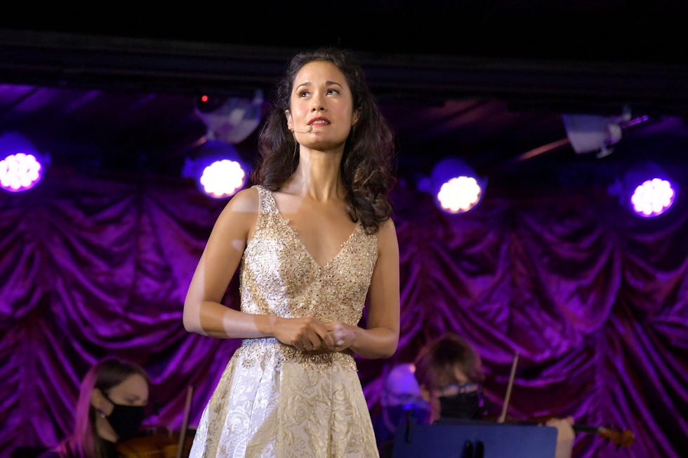 ali ewoldt wearing a white dress, holding her hands together, on a stage with a purple curtain in the background