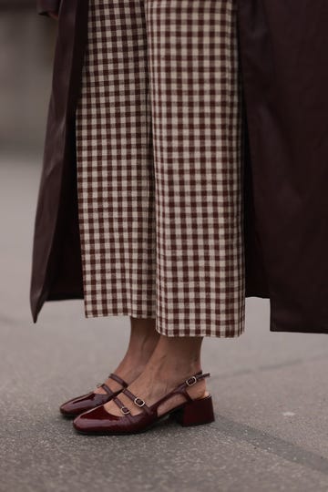 a woman wearing a pair of burgundy mary jane block heels with gingham print pants and a coat on the street in berlin in a roundup of the best heels for wide feet 2024