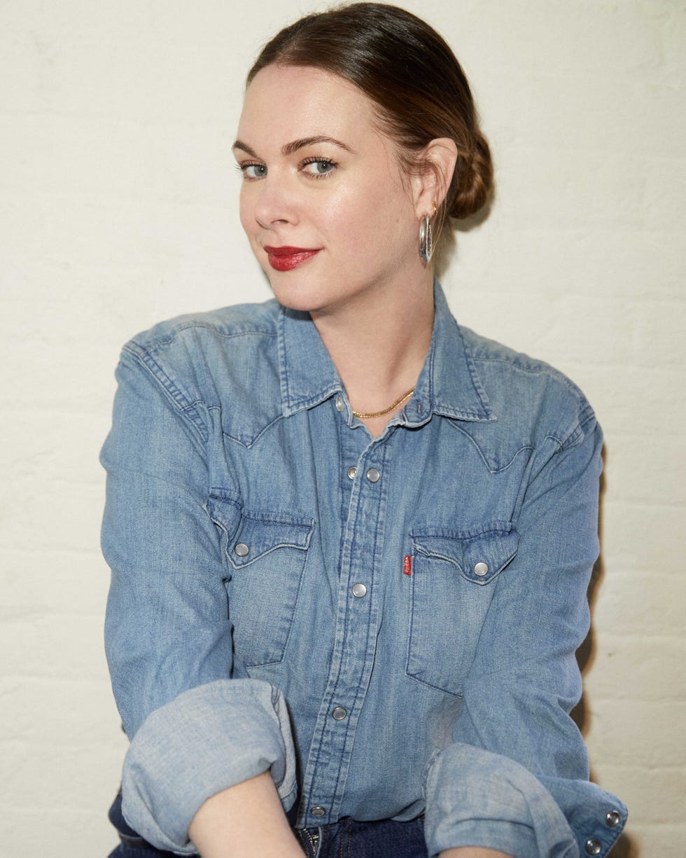 person wearing a denim shirt and hoop earrings against a plain background