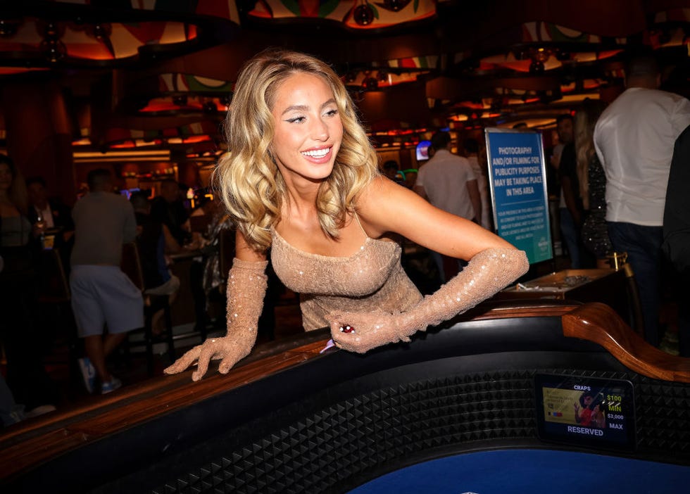 alix earle smiles as she leans against a casino table and prepares to roll dice, she wears a nude sparkly dress and matching elbow length gloves