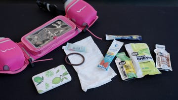 a collection of running accessories and energy nutrition products arranged on a flat surface these include a pink hydration belt with compartments for holding water bottles a small container with a lime design a facial cream tube a hair tie and several packets of energy gels and chews from brands like gu and liquidurance featuring flavors such as salted lime and pineapple a paper napkin is also present in the arrangement