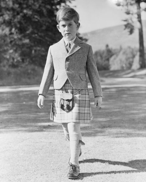 prince charles walks while wearing a kilt, he looks at the camera with a solemn expression