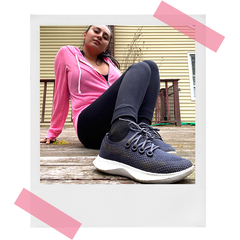 woman wearing pink hoodie showing off allbirds dasher sneakers outside