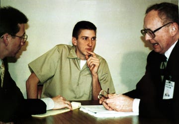timothy mcveigh, wearing a tan prison jumpsuit, listening to two men in suits and glasses at a table