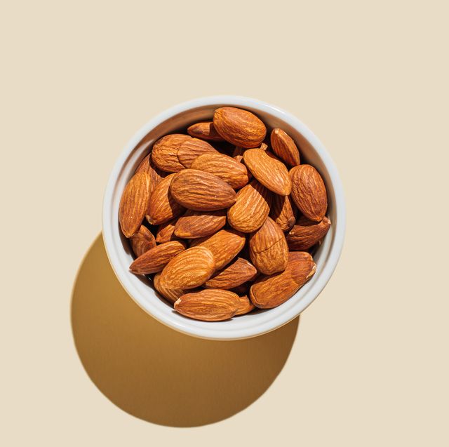 almond nuts in white bowl isolated on beige background minimal flat lay style top view, copy space
