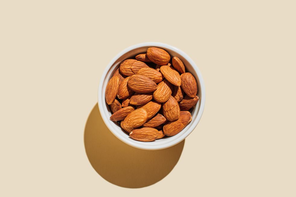 almond nuts in white bowl isolated on beige background minimal flat lay style top view, copy space