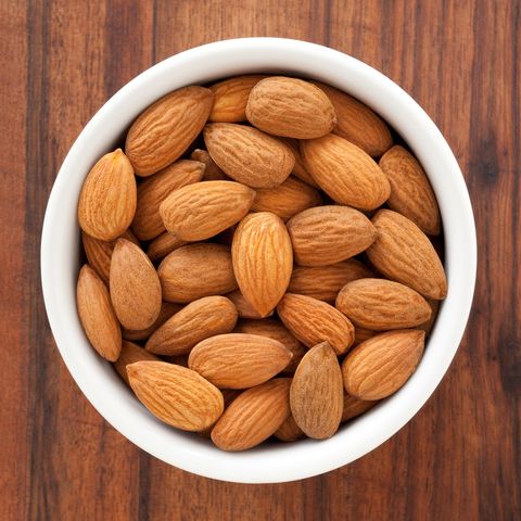 a bowl of almonds on a wooden table, an ingredient in one of good housekeeping's best homemade face scrubs