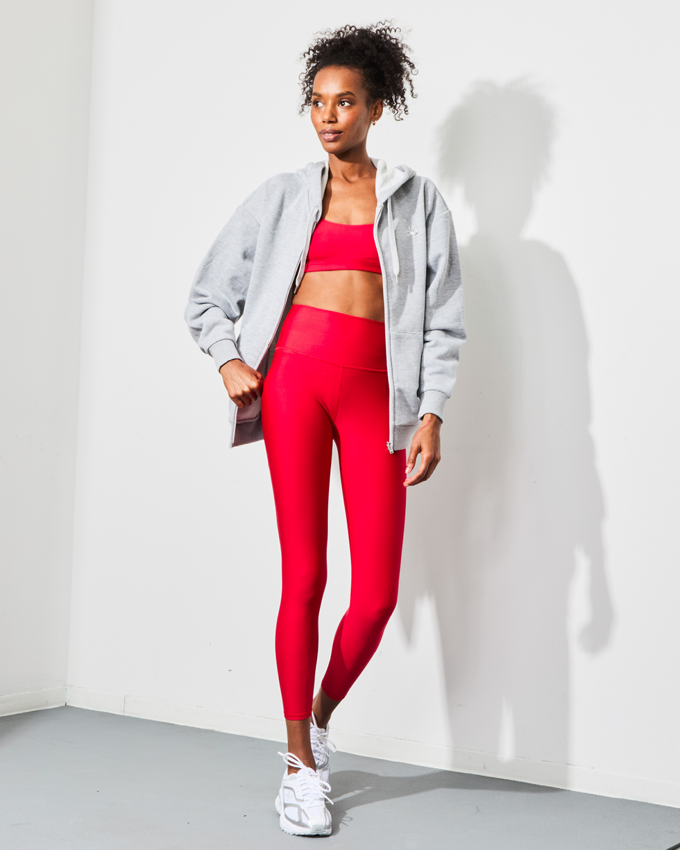 a person dressed in athletic wear including a red sports bra and matching leggings complemented by a light gray hoodie and sneakers