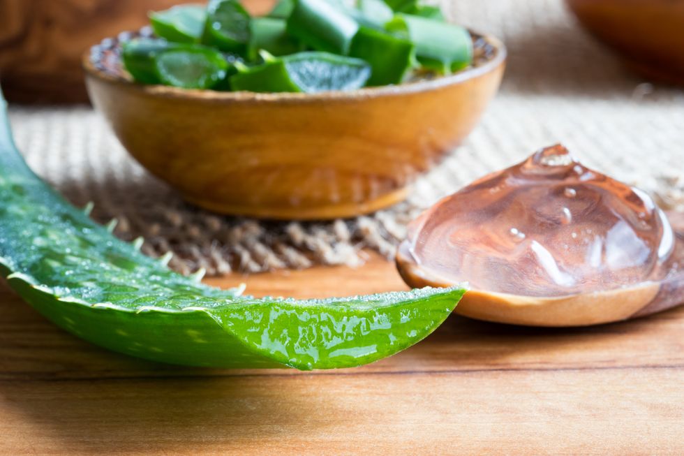aloe vera leaf, with aloe vera gel and slices in the background