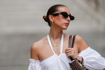 paris, france may 12 gabriella berdugo wears sunglasses, earrings, golden jewelry, a necklace in gold with pearls, a heart shaped necklace, a white off shoulder linen gathered dress from kalita with balloons  puff sleeves, a brown summer bag from carolina herrera in brown leather, during a street style fashion photo session, on may 12, 2024 in paris, france photo by edward berthelotgetty images