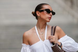 paris, france may 12 gabriella berdugo wears sunglasses, earrings, golden jewelry, a necklace in gold with pearls, a heart shaped necklace, a white off shoulder linen gathered dress from kalita with balloons  puff sleeves, a brown summer bag from carolina herrera in brown leather, during a street style fashion photo session, on may 12, 2024 in paris, france photo by edward berthelotgetty images