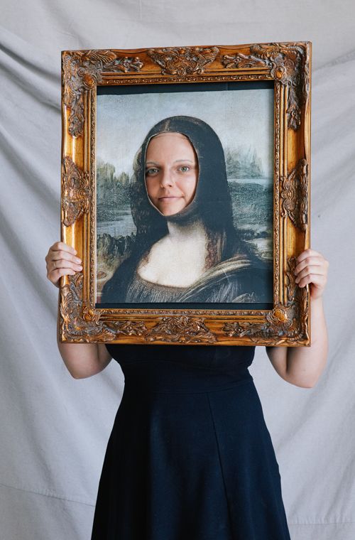 woman holding framed picture of the mona lisa with the face cut out over her own face