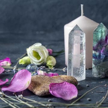 a white candle surrounded by various crystals, flower petals, and stones