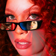 woman with curly red hair peers over sunglasses