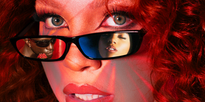 woman with curly red hair peers over sunglasses