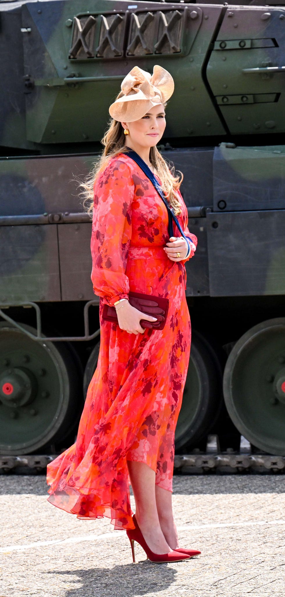amalia de holanda, con el brazo en cabestrillo, un vestido en tonos rojos y naranjas y zapatos de tacon alto