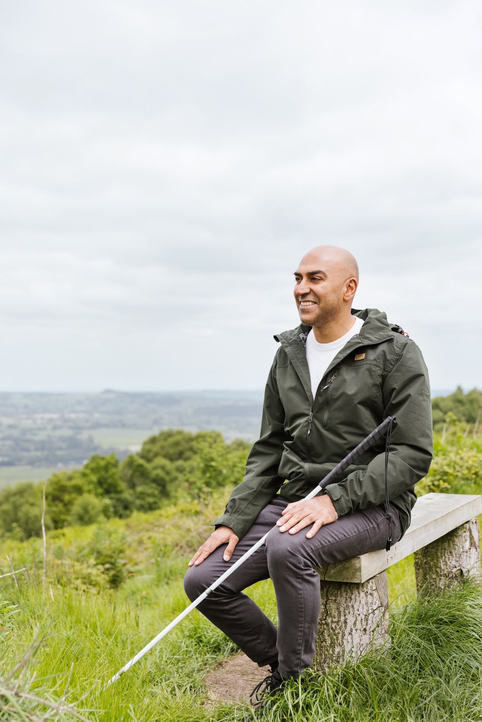 amar latif sitting on a bench in the countryside he is smiling and overlooking the green rolling hills