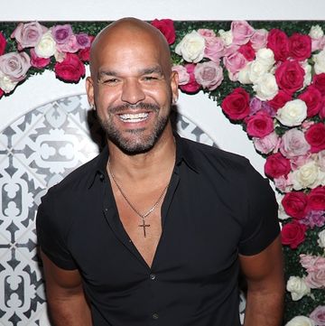 amaury nolasco wears a black outfit and poses in front of a flower wall in december 2021