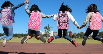 group of children jumping together while holding hands each wearing a colorful backpack