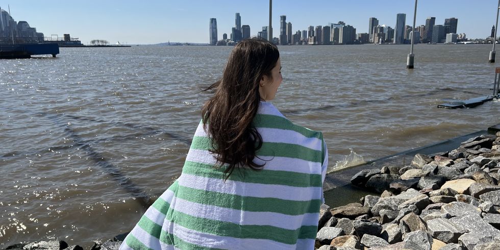 a model wearing a green and white amazon basics cabana stripe beach towel across her shoulders, good housekeeping's best beach towels