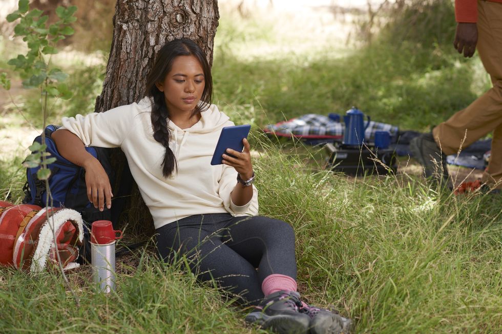 a woman sat in a park holding a kindle paperwhite in denim