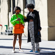 two women standing in front of a building and looking at their phones two women standing in front of a building and looking at their phones